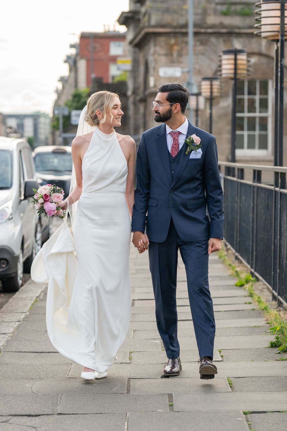 Elegant couple in wedding attire walking together on a cobblestone street.