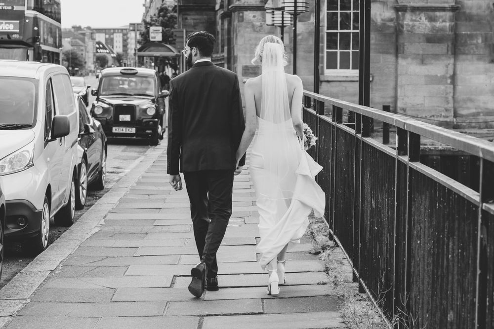 Black and white photo of newlyweds walking down a city street from behind.