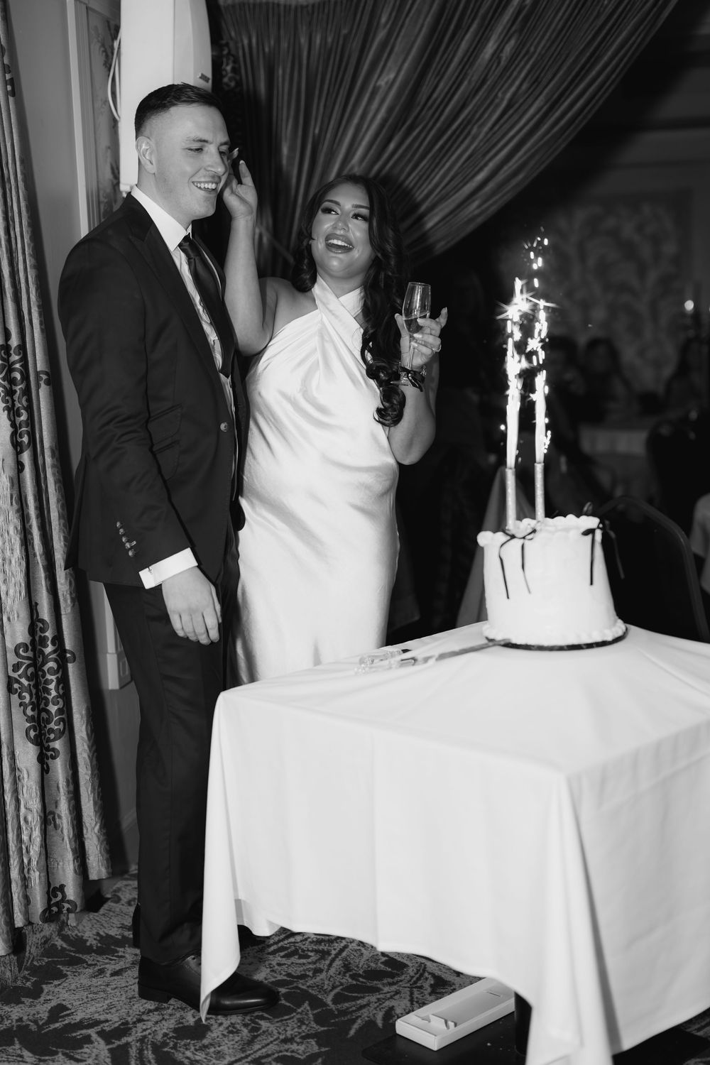 Black and white photo of couple celebrating by wedding cake with sparkler decoration.