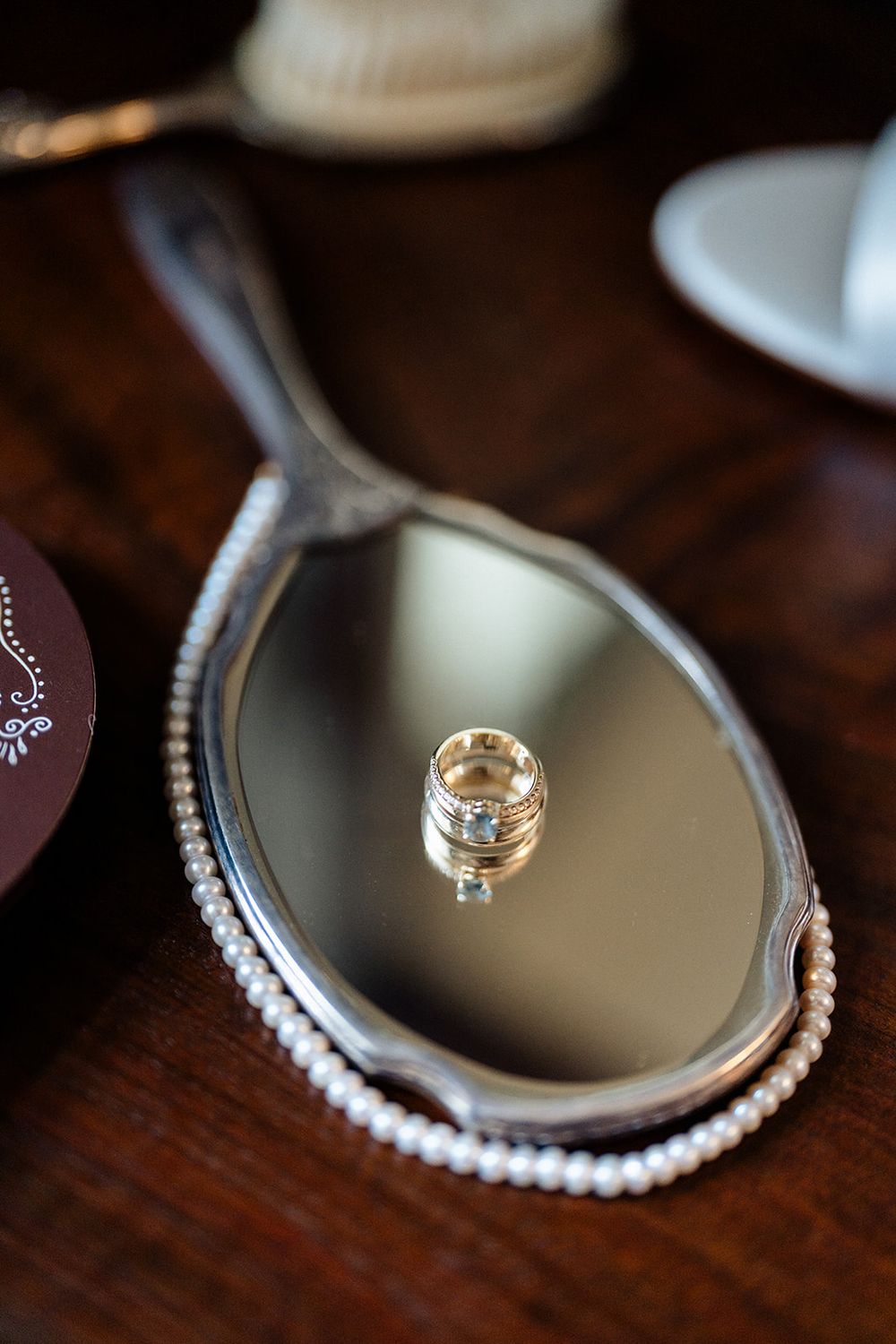 A series of close-up shots showing wedding rings and pearls arranged on a reflective mirrored surface.