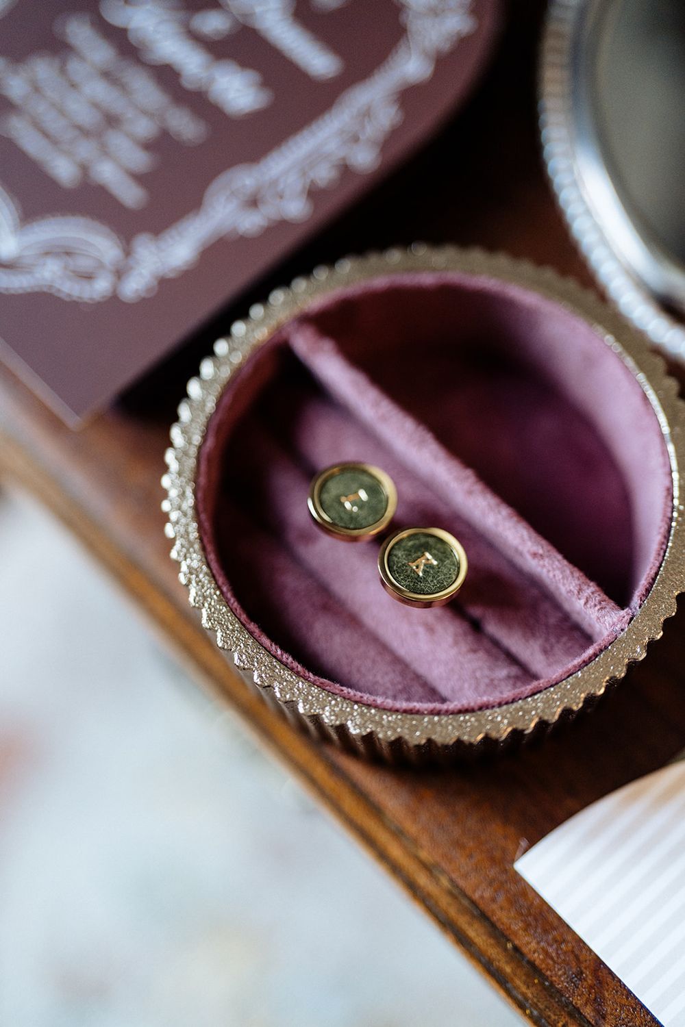 Gold wedding band resting on a round purple velvet ring cushion with delicate lace trim.
