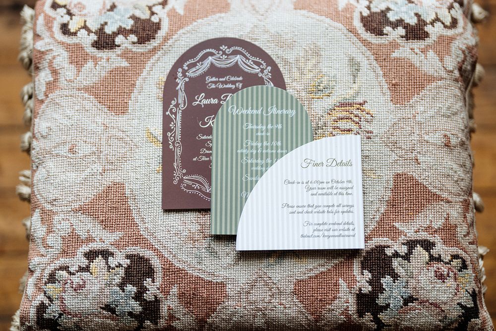 Wedding invitation cards displayed on a decorative lace pillow in brown and white tones.