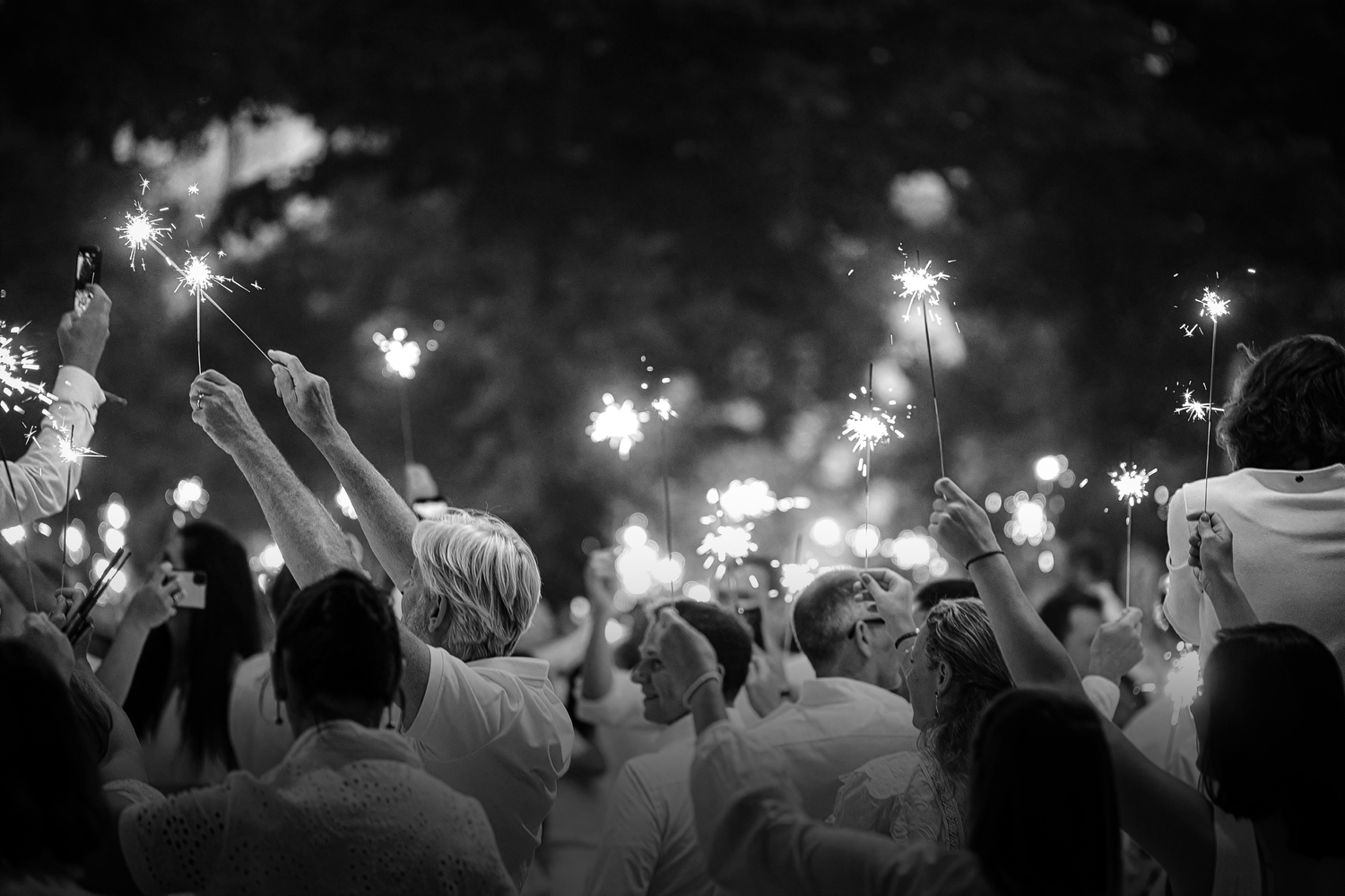 Crowd of people in white clothing holding sparklers aloft at an outdoor nighttime celebration.