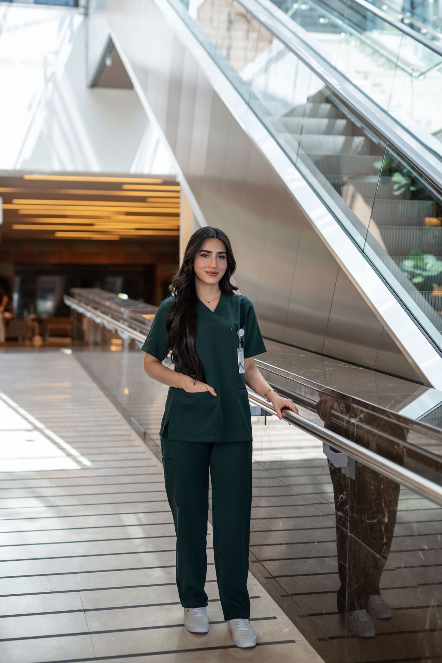 Healthcare worker in green scrubs poses on modern staircase in medical facility.