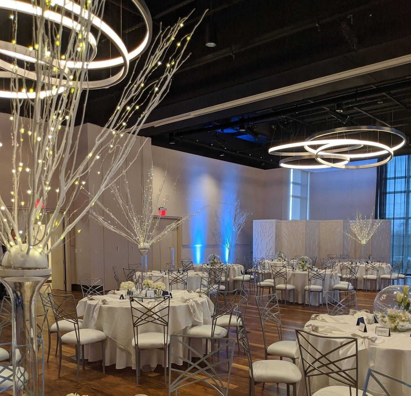Wedding reception ballroom with illuminated branch centerpieces and white and silver decor.