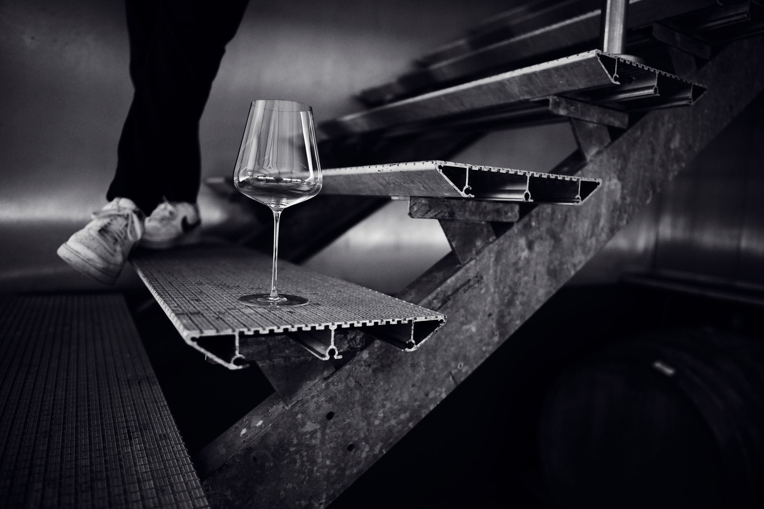 Dramatic black and white photo of an empty wine glass balanced on metal cellar stairs.