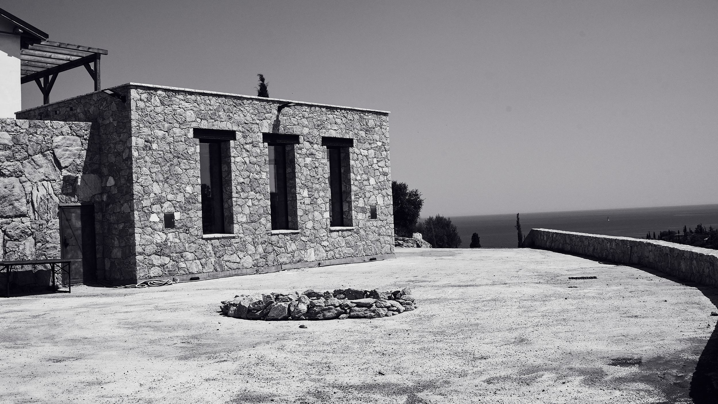 Stone building with arched windows on a hilltop overlooking the sea, black and white landscape.