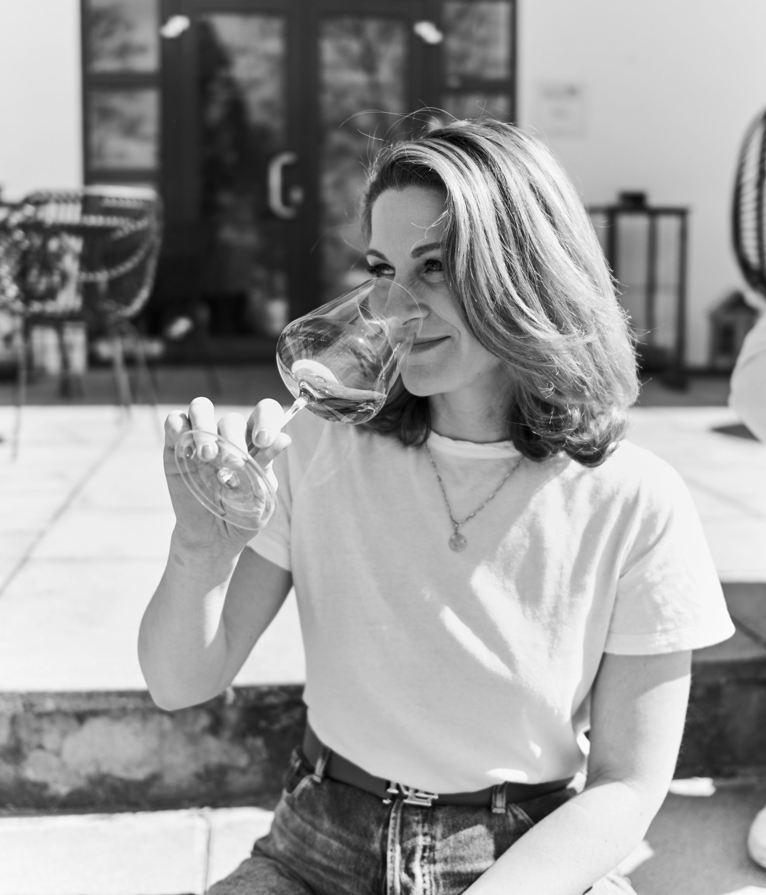 Young woman in white t-shirt tasting wine from a large glass outdoors, black and white photo.