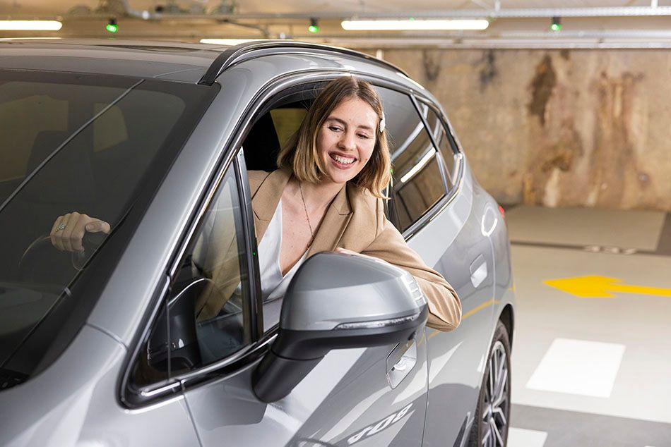 Woman driving a silver car through an indoor parking garage.
