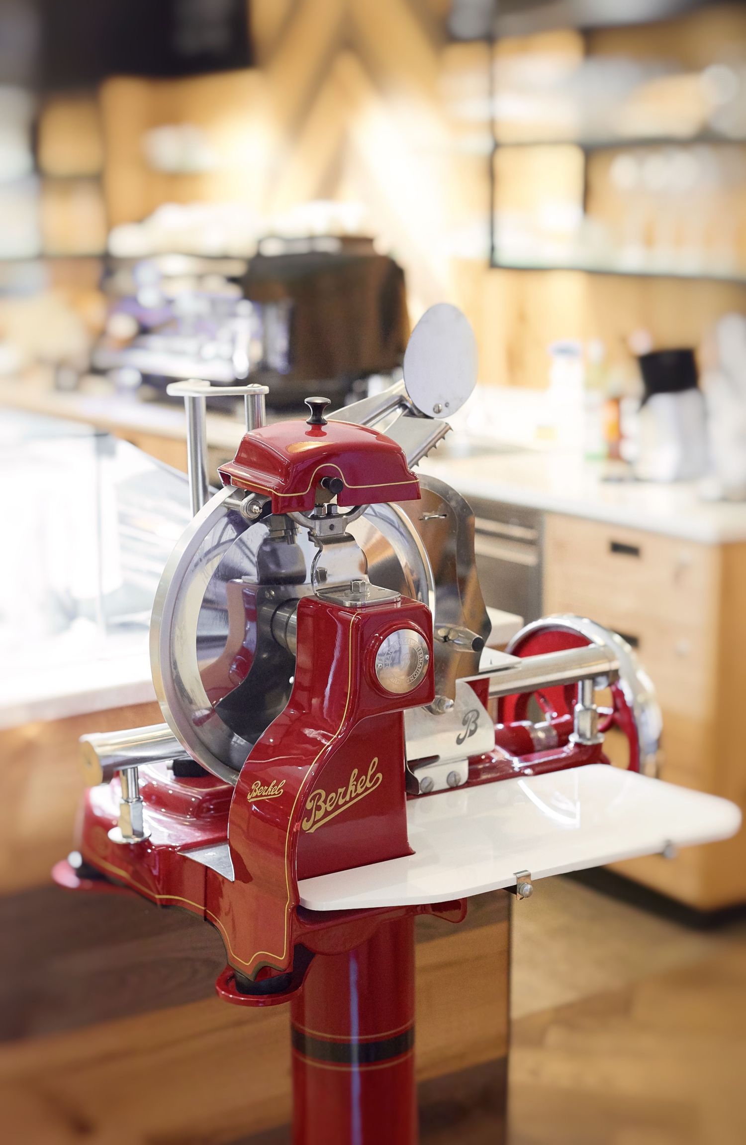 Vintage red Berkel meat slicer on pedestal stand in a modern kitchen or deli setting.