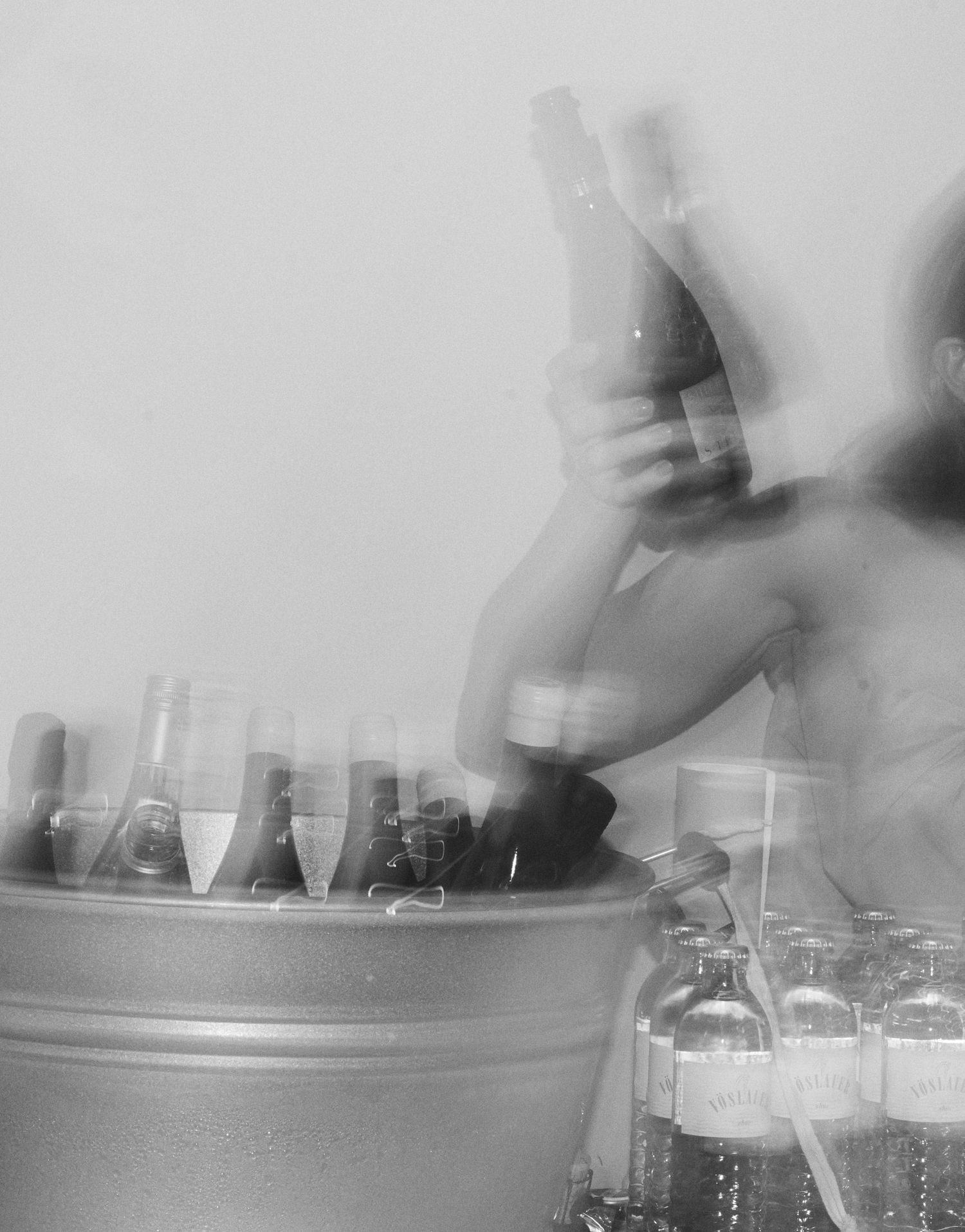 Blurred black and white image of person retrieving champagne bottle from ice bucket at bar.