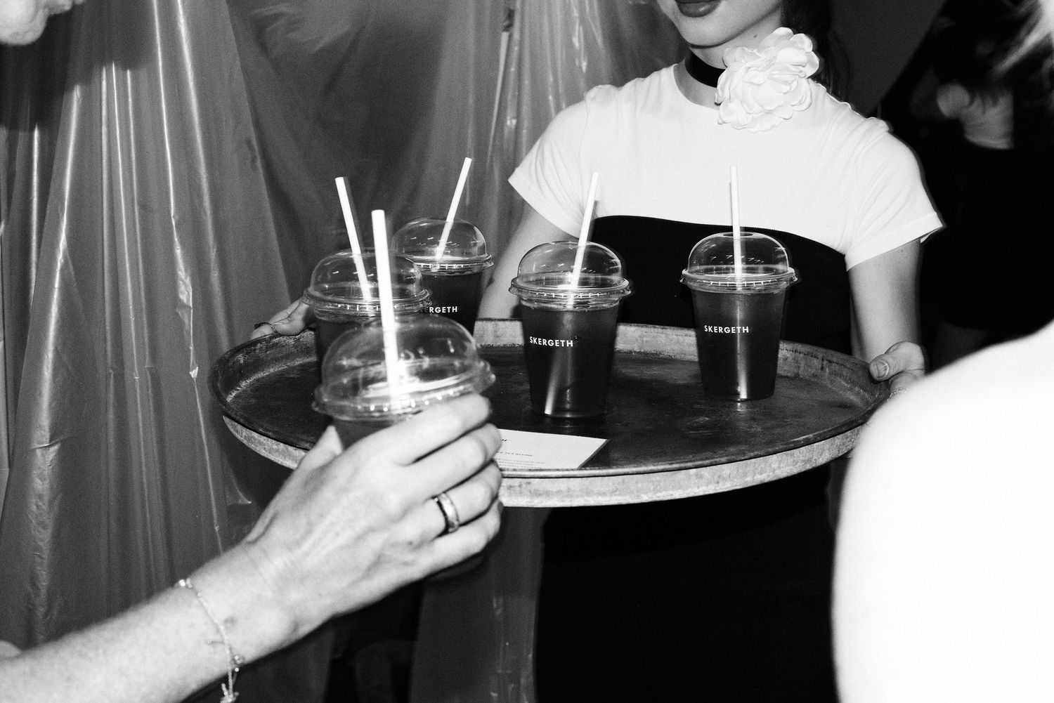 Black and white photo of server holding tray of iced drinks being handed to guests at event.