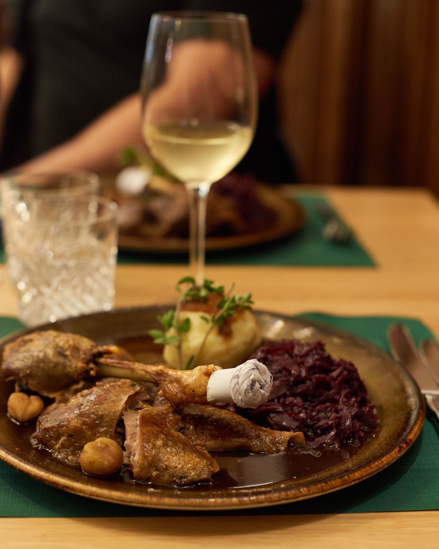 Traditional roasted game dish with red cabbage and dumplings served on rustic plate with white wine.