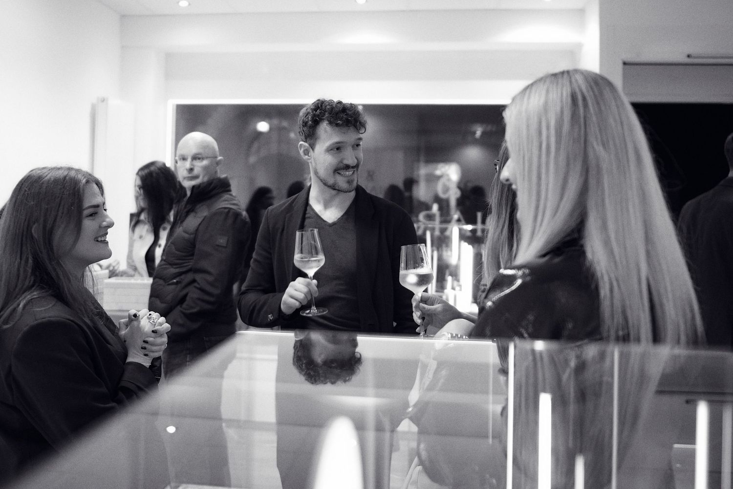 Three guests socializing with wine glasses at elegant black and white indoor reception.