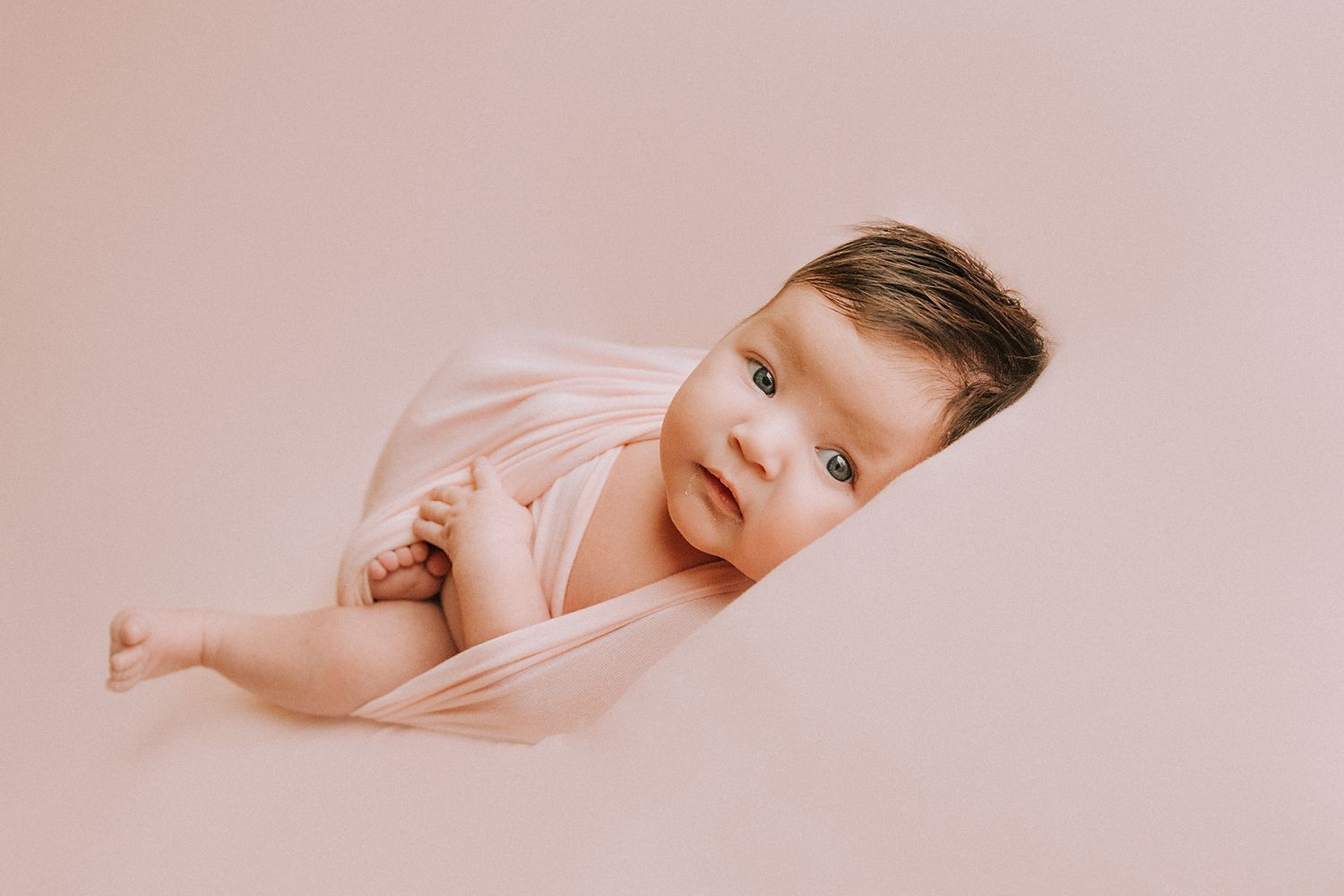 A sleeping baby rests peacefully on soft pink bedding in a minimalist composition.
