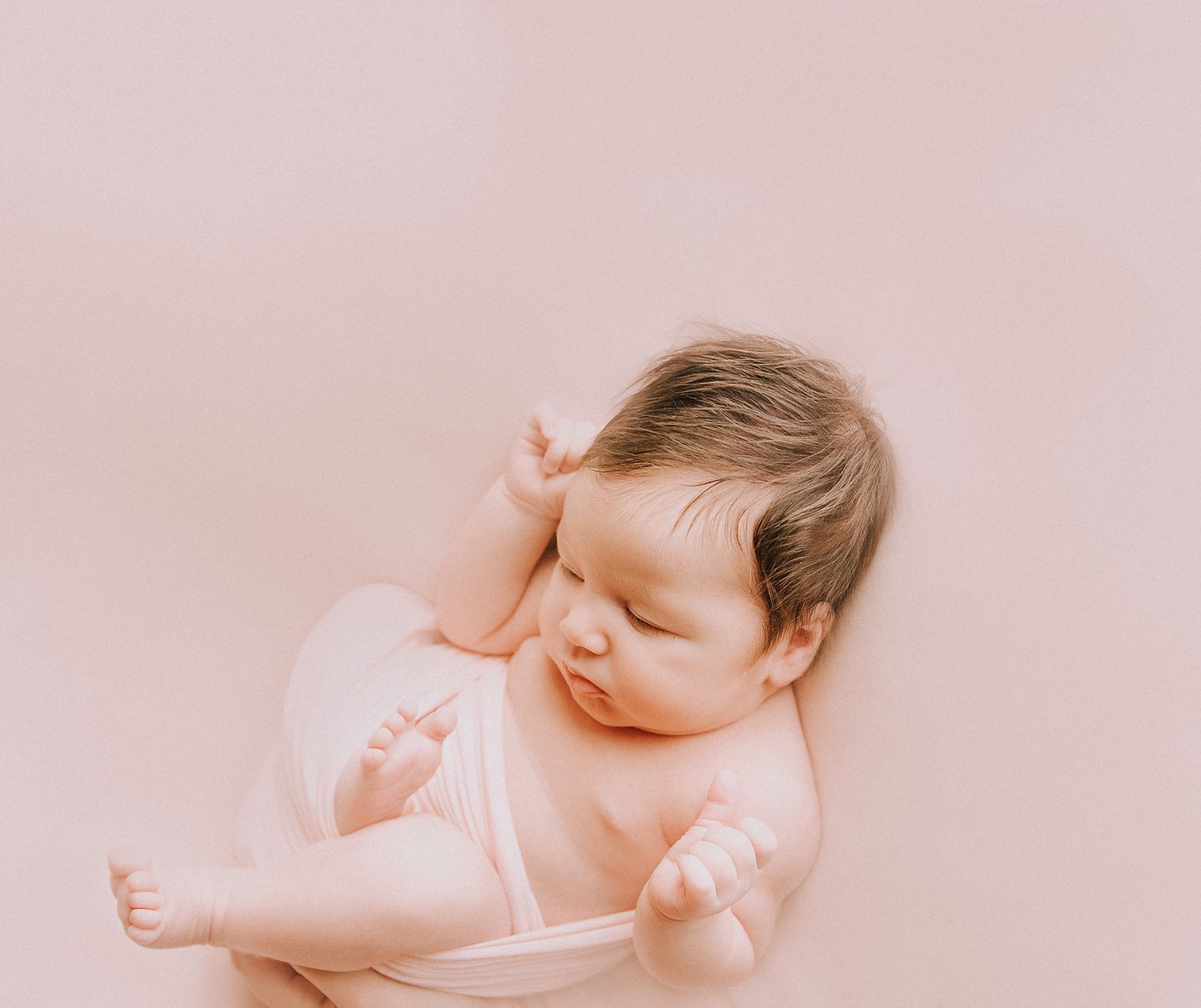 Sleeping newborn baby wearing delicate lace bonnet on soft pink background.