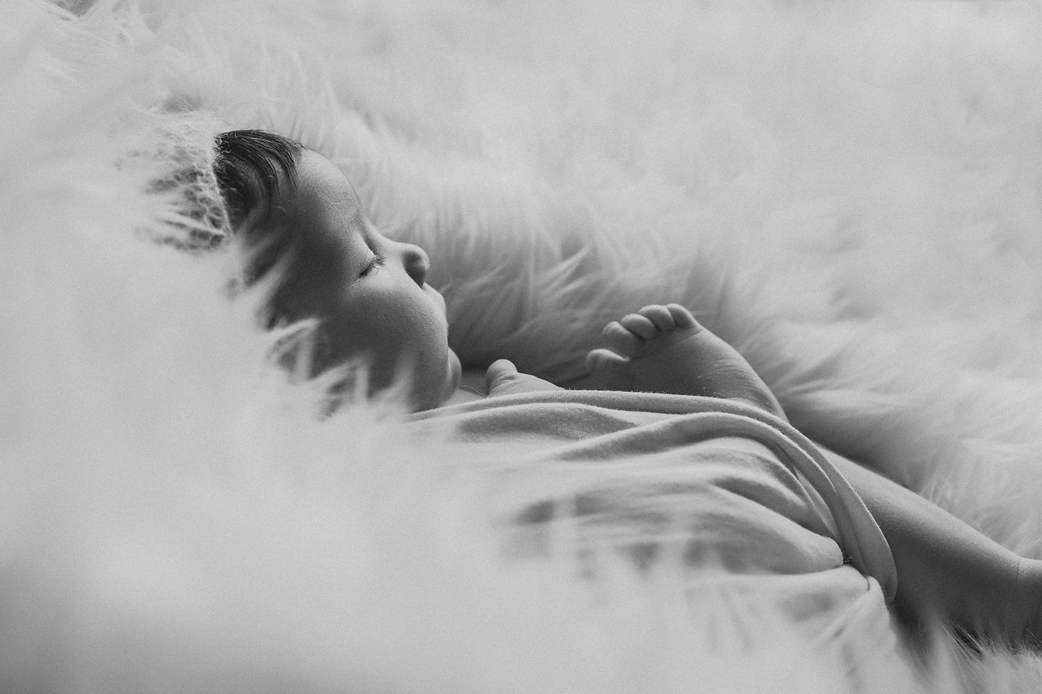 Artistic black and white portrait of sleeping baby on soft textured surface.