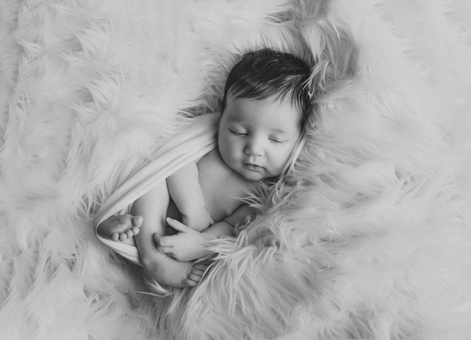 Peaceful sleeping newborn baby lying on soft white feathery blanket in black and white photography.