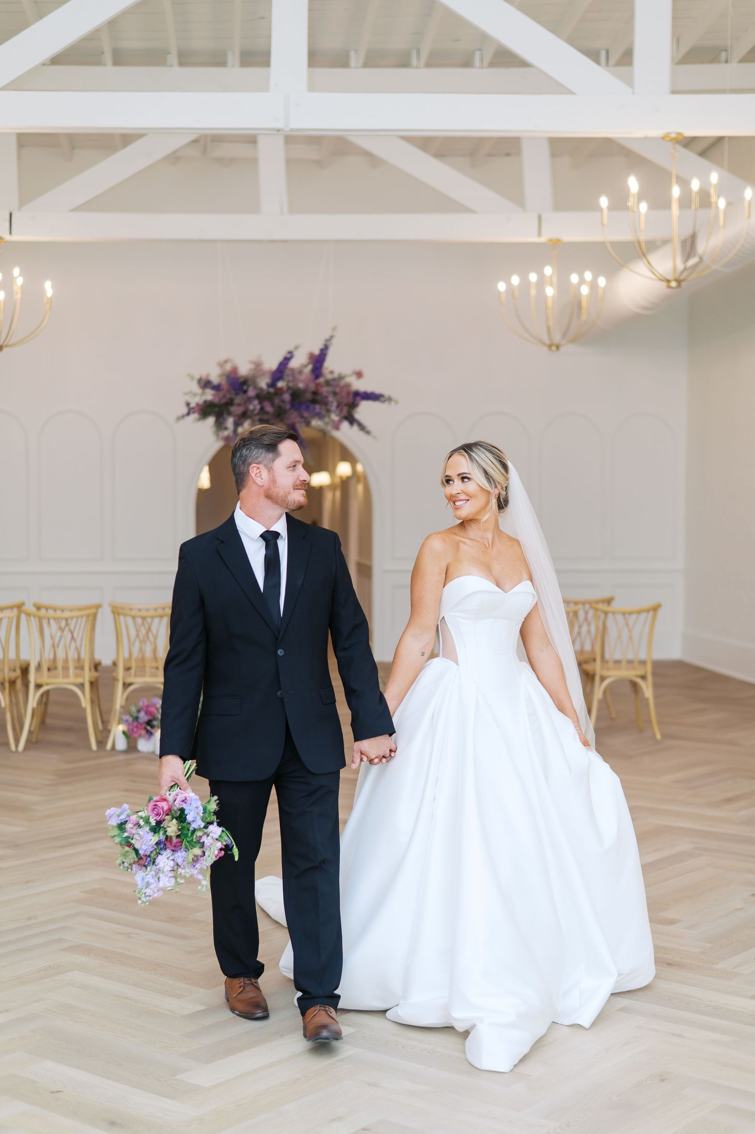 A wedding couple walks together in a bright white venue with herringbone wood floors in downtown fayetteville NC by wedding photographer