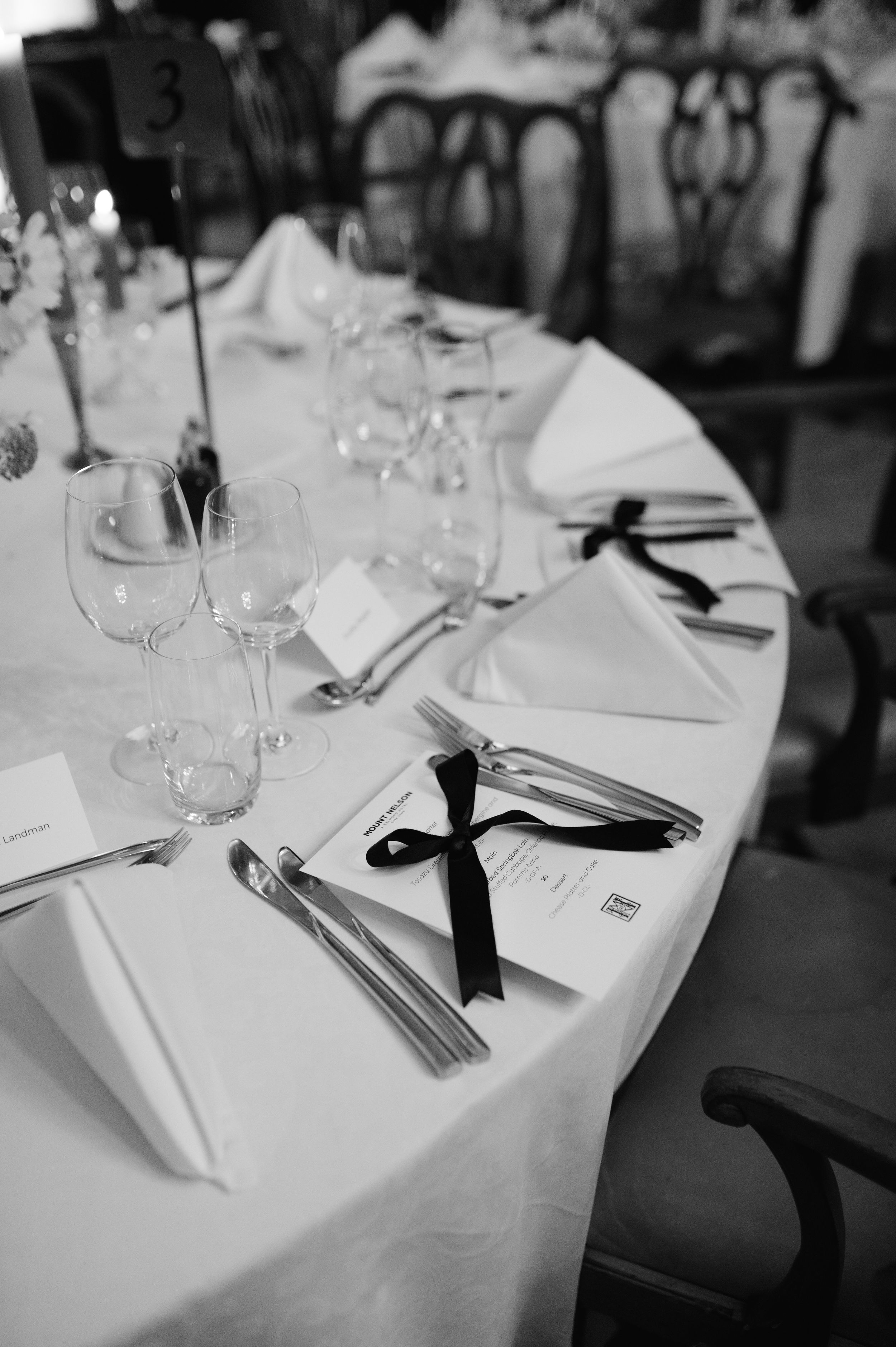 Elegant table settings with white linens, wine glasses, and black ribbon accents at a formal event.