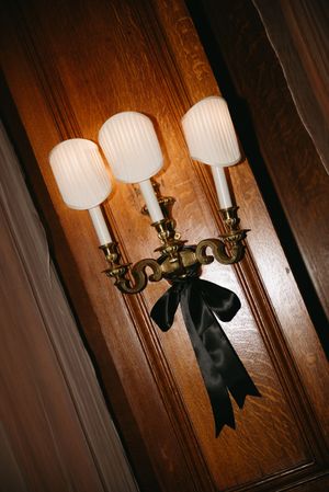Vintage wall sconce with ornate brass details and white glass shades adorned with black ribbon.