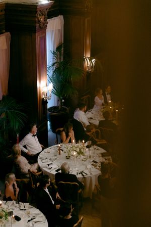 Guests seated at elegant dining tables in a dimly lit restaurant with ambient lighting and decorative palm plants.