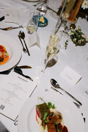 Wedding reception table settings with white linens, wine glasses, and plated gourmet meals.
