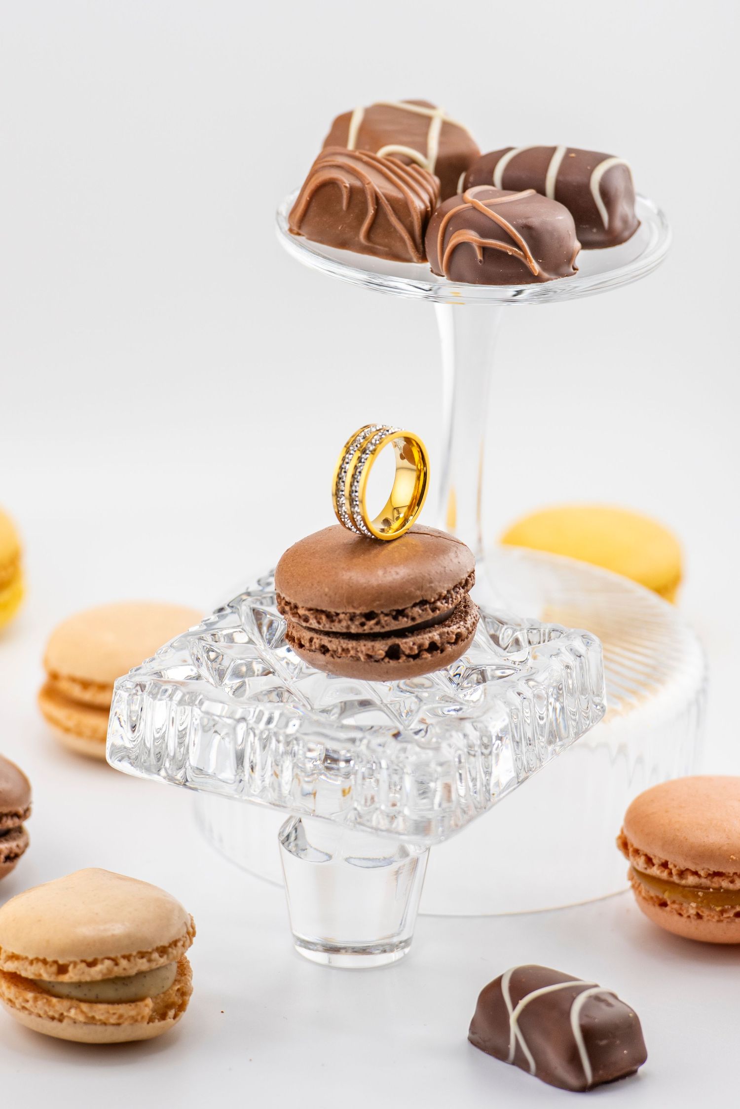 Elegant display of chocolate truffles and pastel macarons on crystal glass pedestals against a white background.