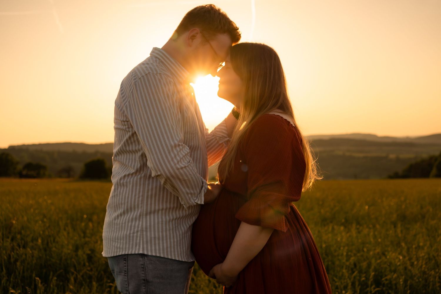 A couple embraces in a golden wheat field at sunset creating a romantic silhouette against the glowing sky.