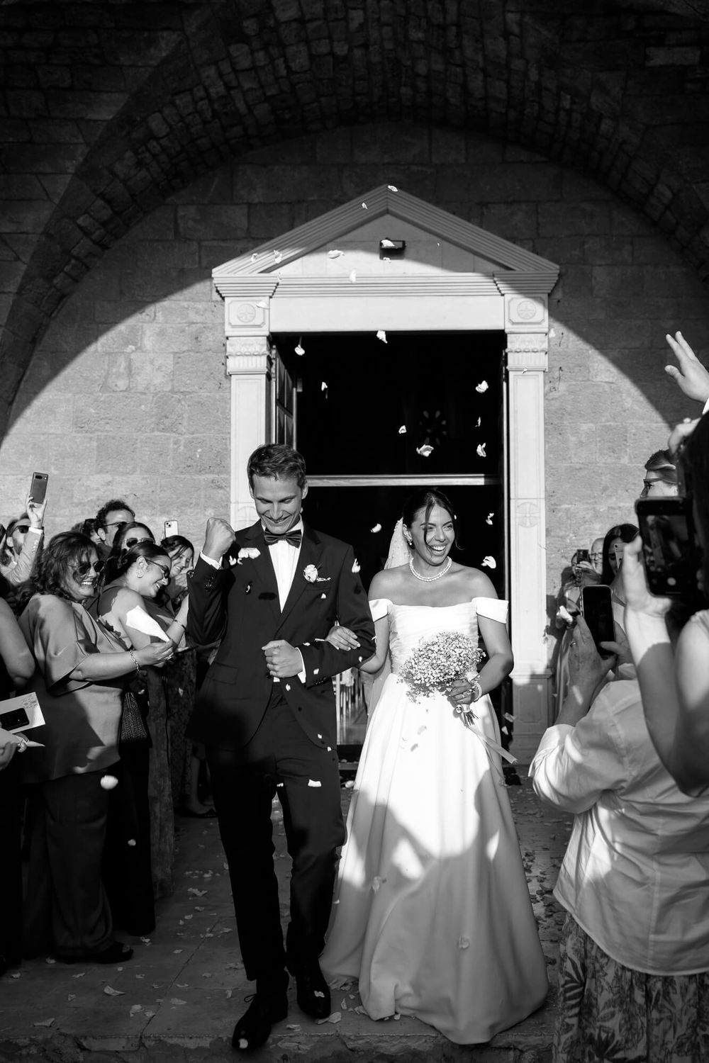 Bride and groom walk out of church as guests toss confetti during joyful wedding ceremony exit.