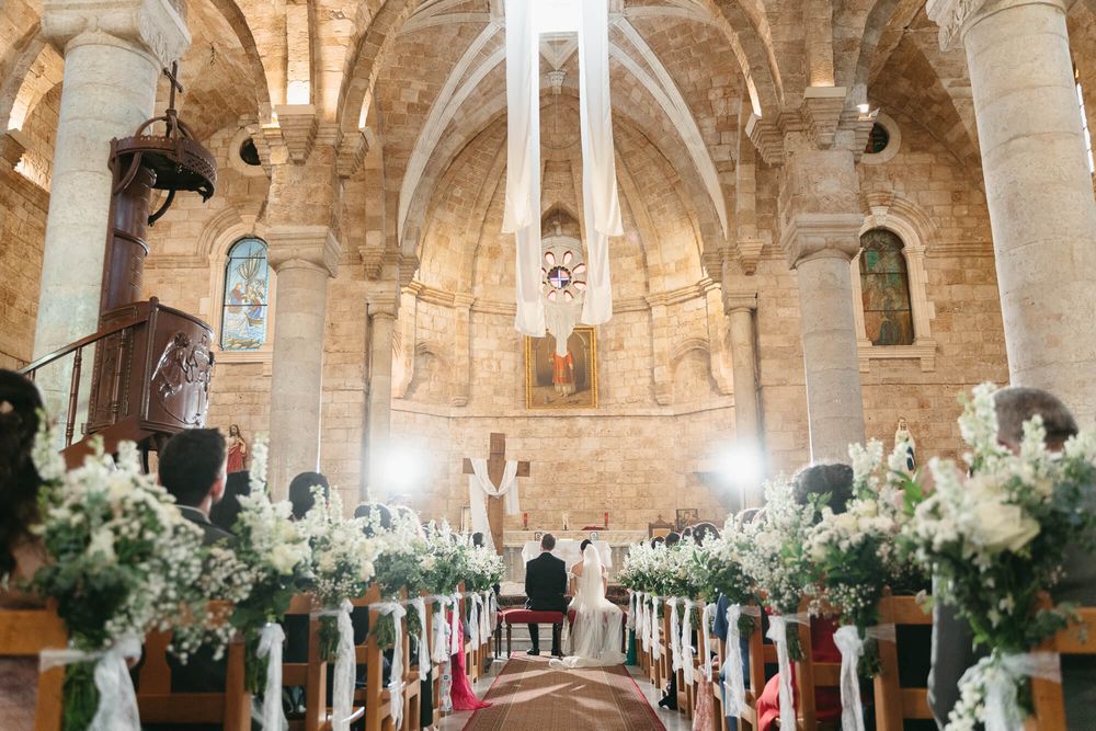 Elegant church wedding ceremony with floral arrangements lining the aisle of a historic stone chapel.