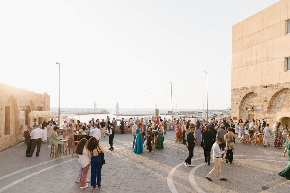 Elegant outdoor wedding reception at a Mediterranean waterfront venue with guests mingling at golden hour.