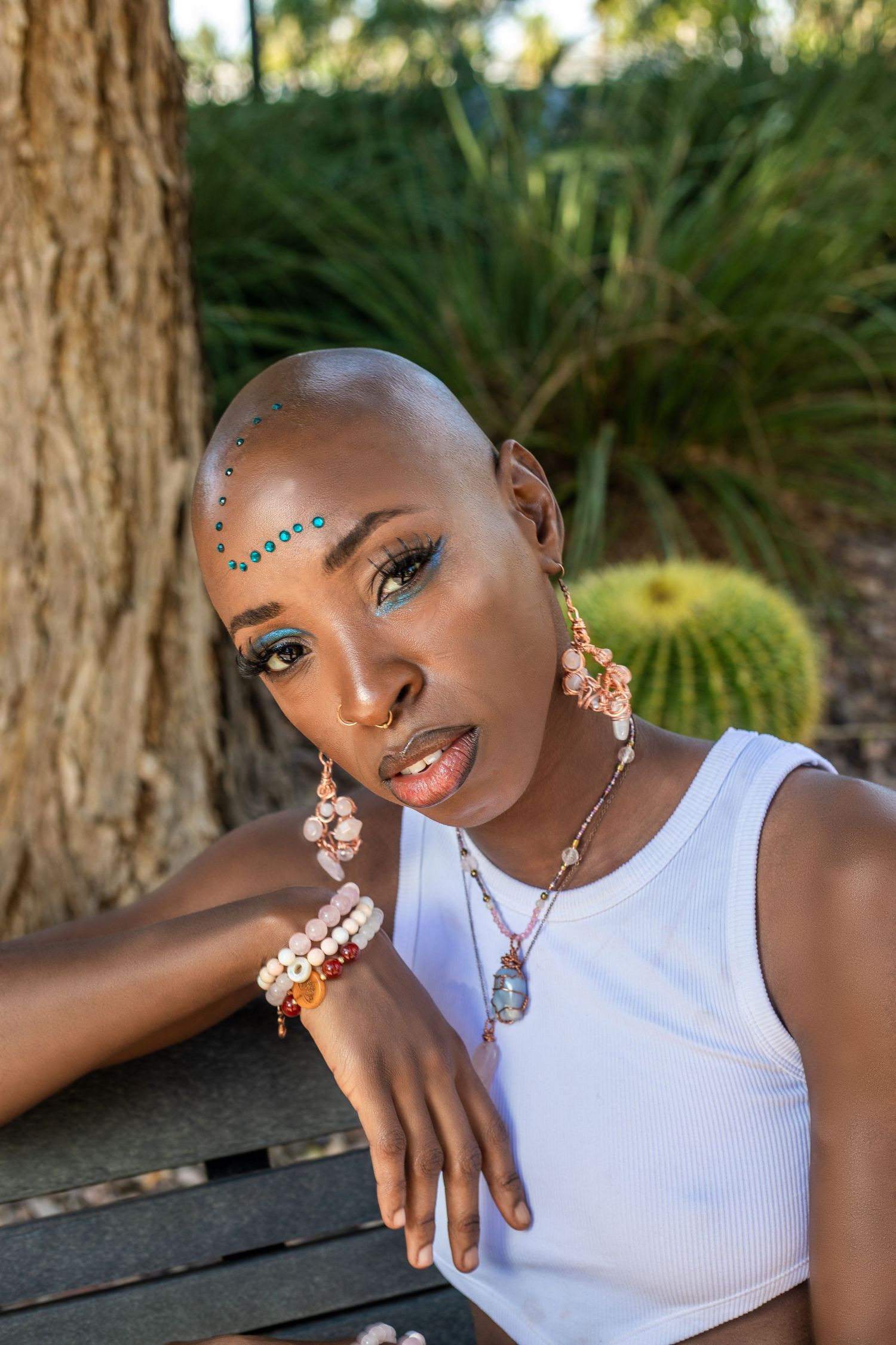 Portrait series showing artistic makeup with blue gems and white tank top against natural background. Jordii's Gems, Woman owned business