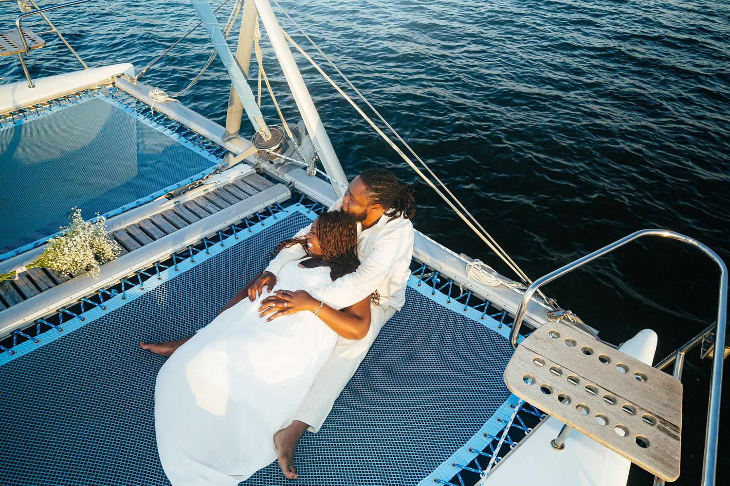 Sailboat cruising on deep blue ocean waters with white sails billowing in the wind and deck visible from above.