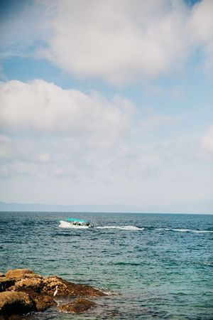 A speedboat cruises across blue ocean waters near rocky coastline under partly cloudy skies.