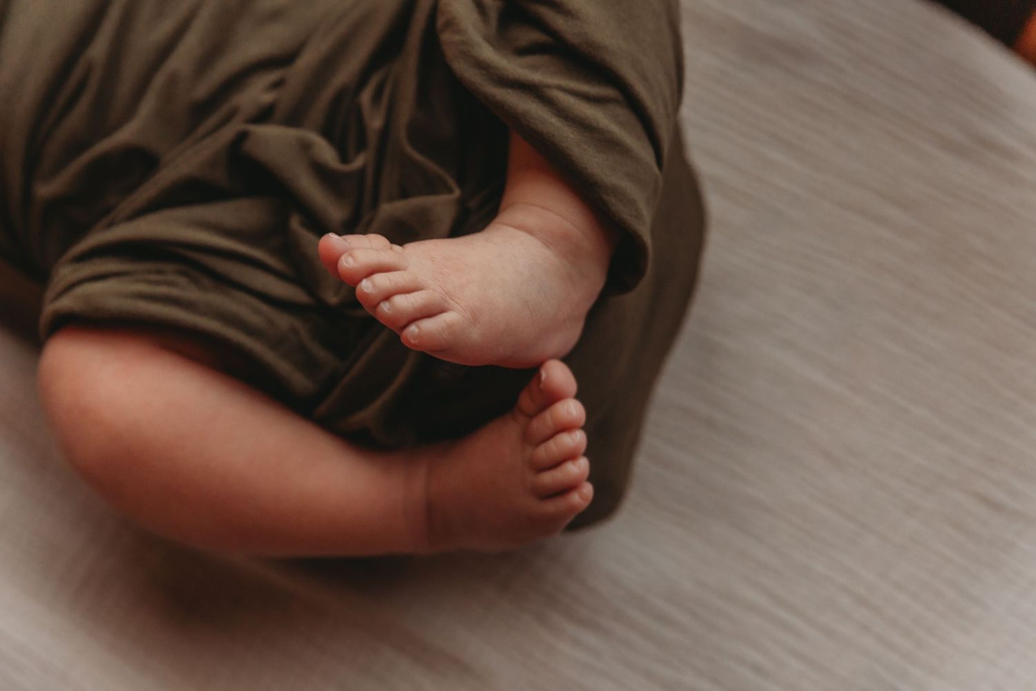Tiny baby feet peek out from brown swaddle blanket against grey background.