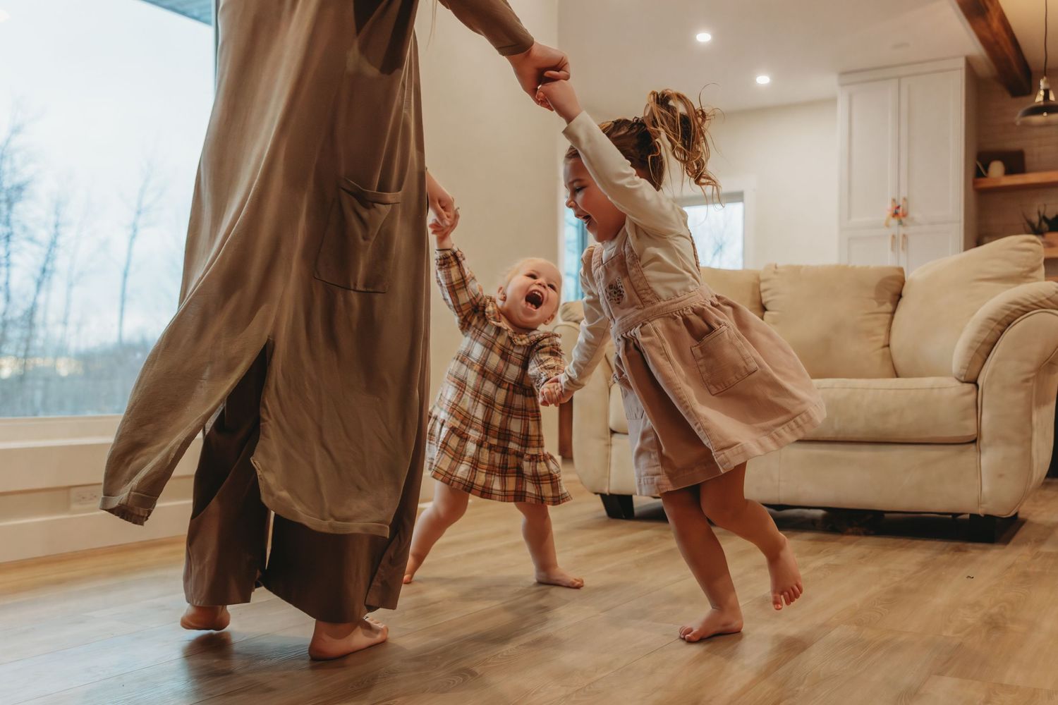 Family dancing together in bright living room with large windows.