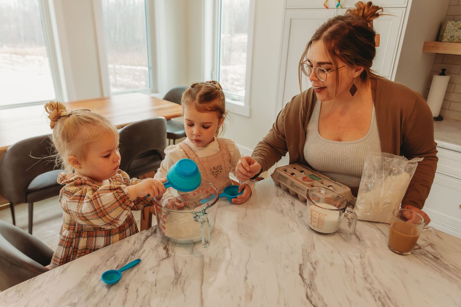 Family cooking and baking together at marble kitchen counter with mixing bowls.