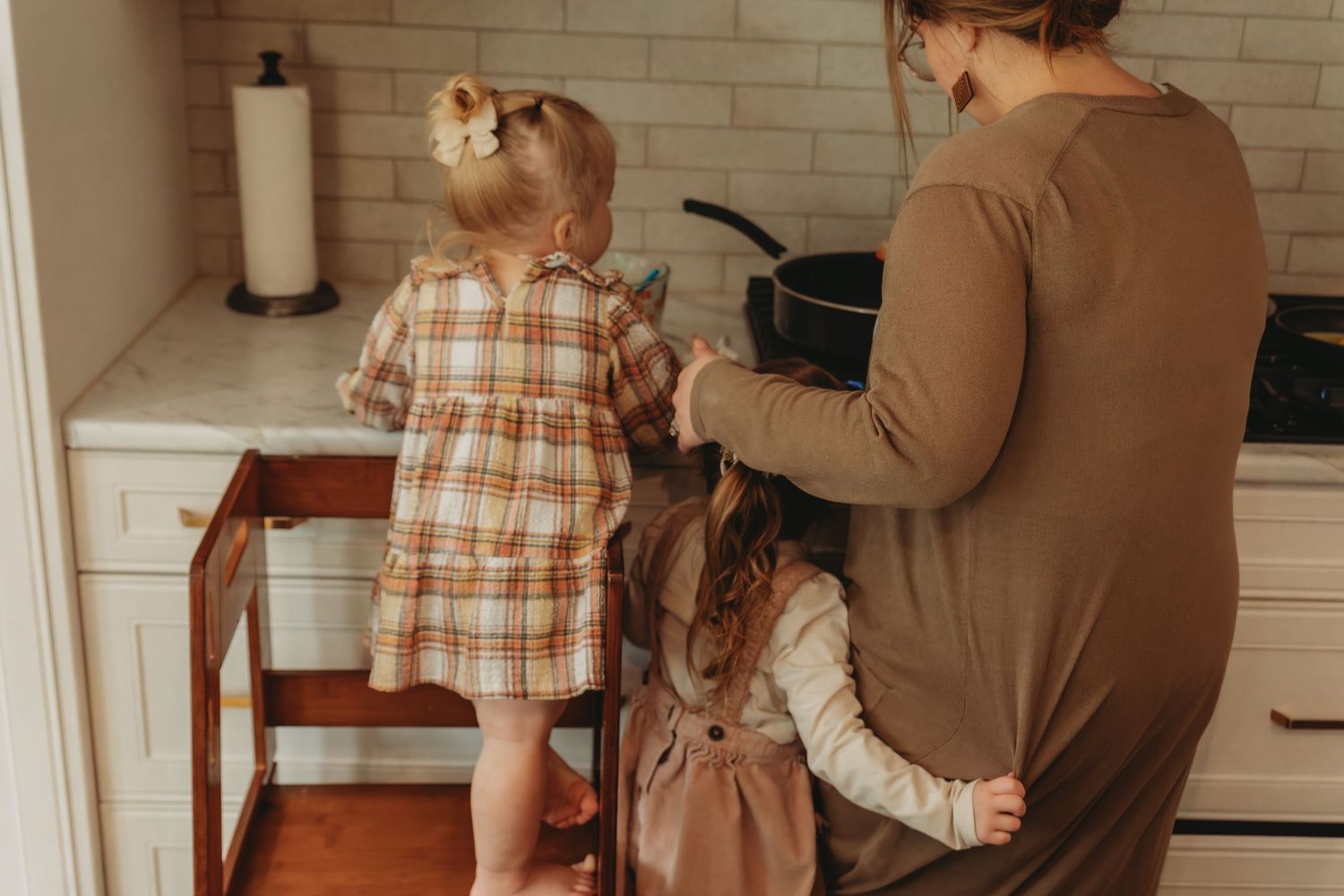 Family working together in kitchen with learning tower and white subway tile backsplash.