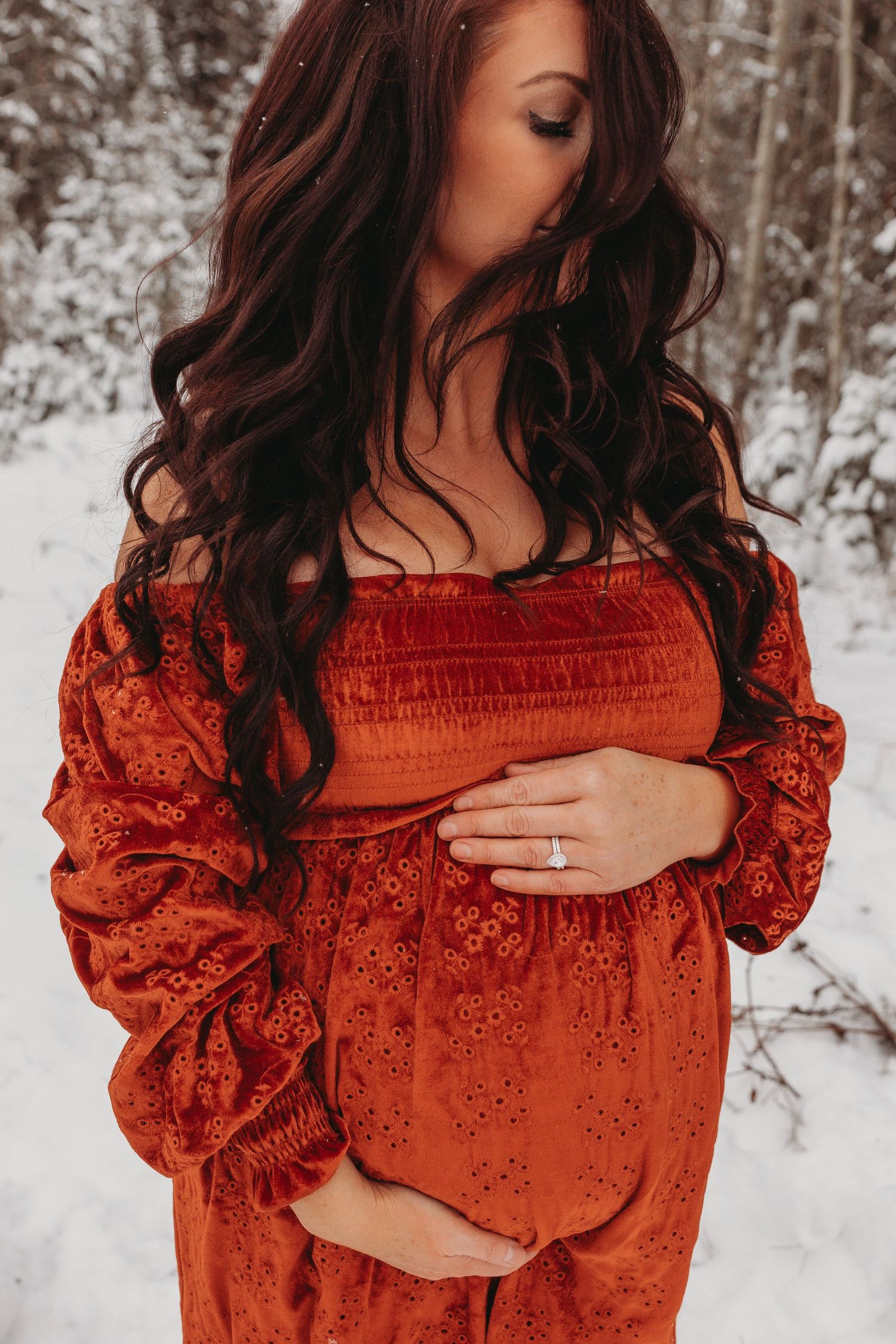 Maternity a red velvet dress with long dark curls against winter scenery.