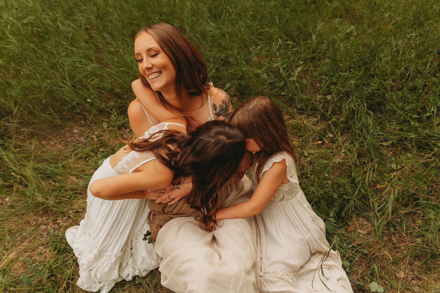 Tender family moment captured outdoors with flowing white dresses against natural backdrop.