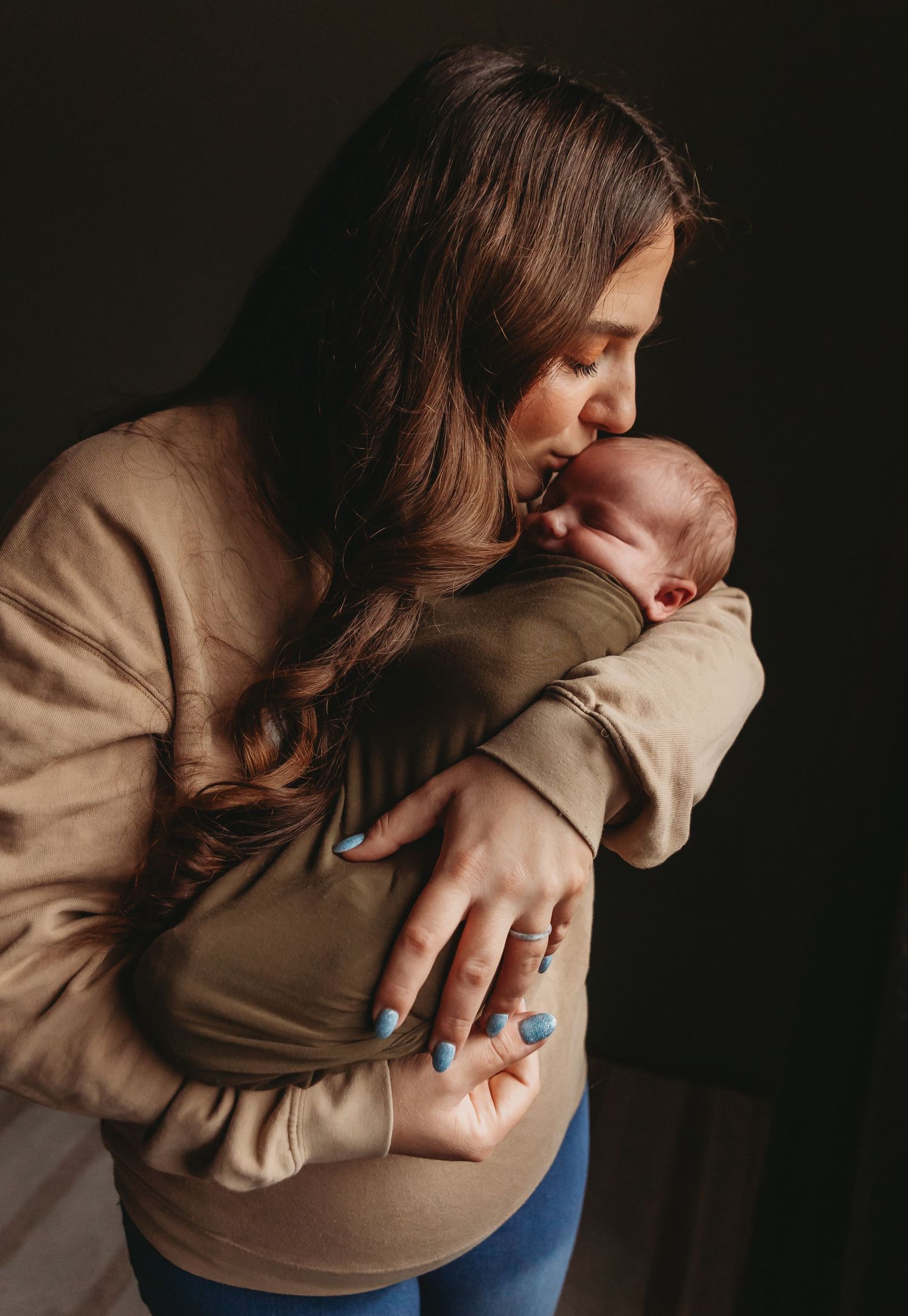 Tender moment captured in soft lighting with newborn in neutral tones.