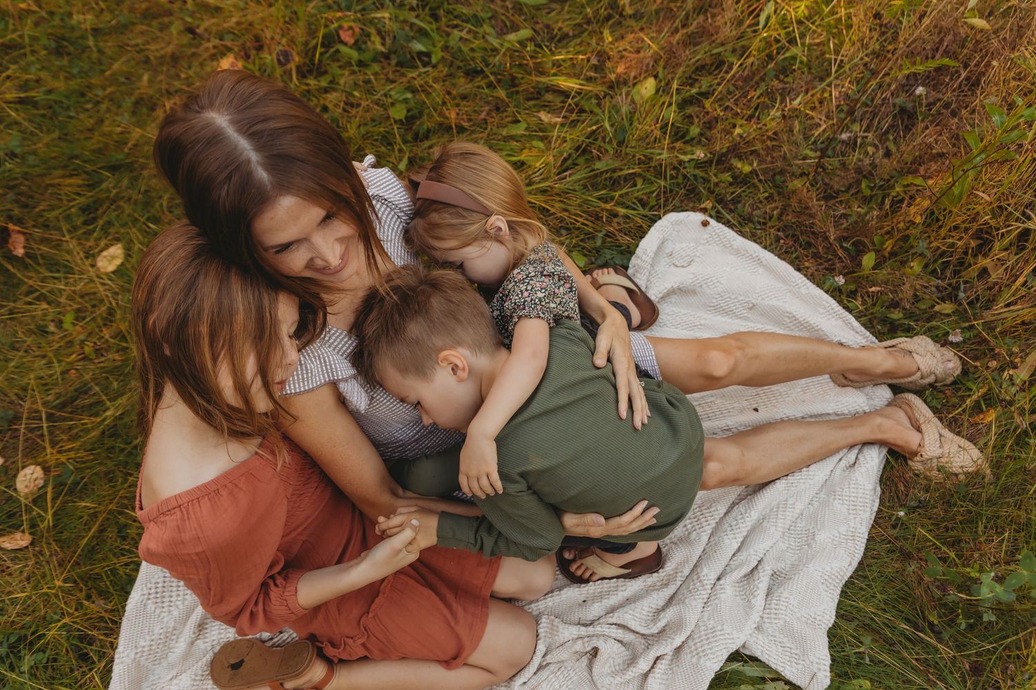 An intimate family moment captured on a blanket in a sun-dappled forest setting.