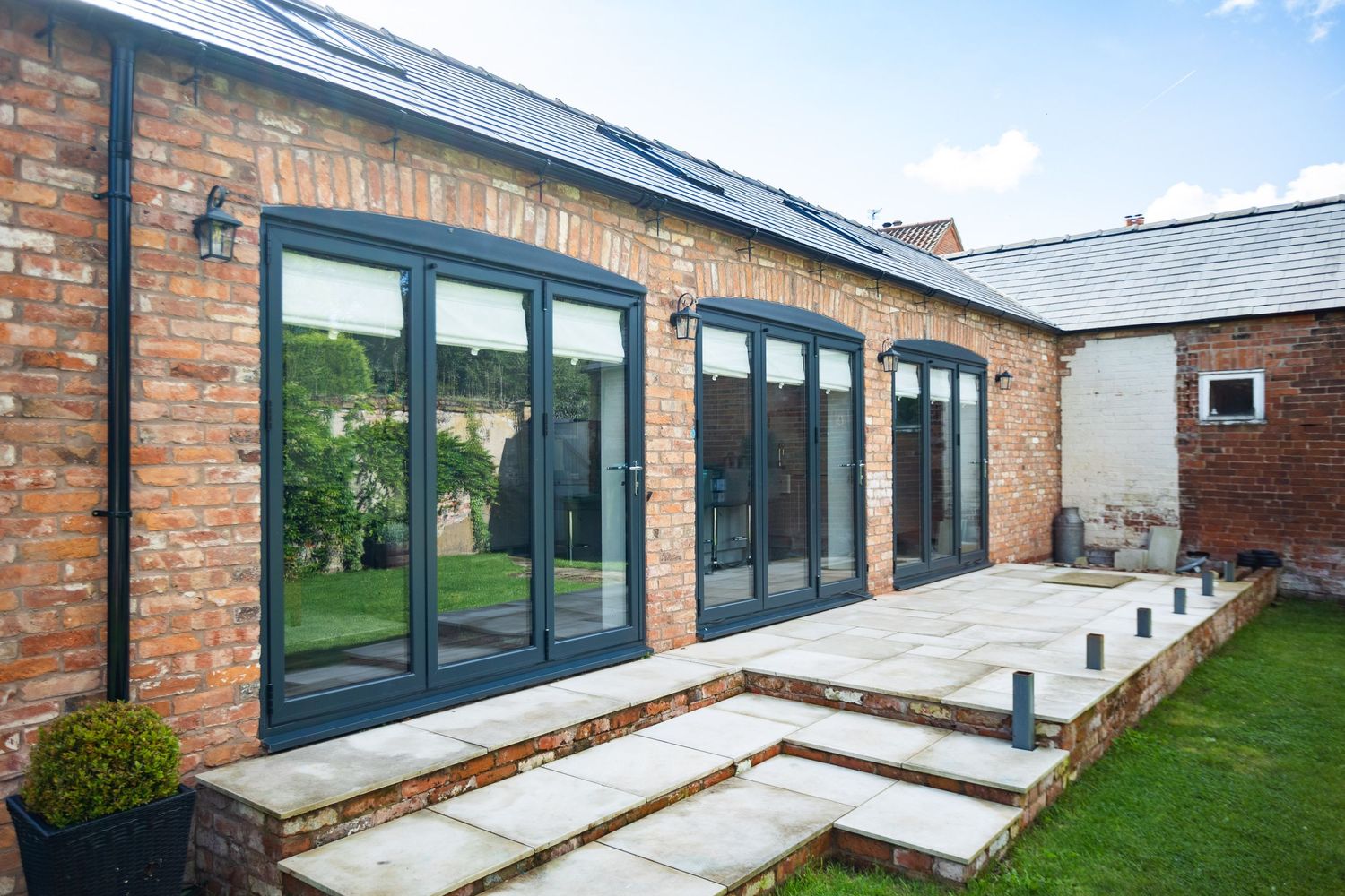 Modern brick building extension with black-framed bifold doors and stone patio steps.