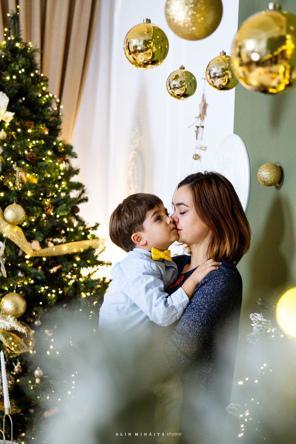 Intimate holiday moment with Christmas tree and gold ornaments in background.
