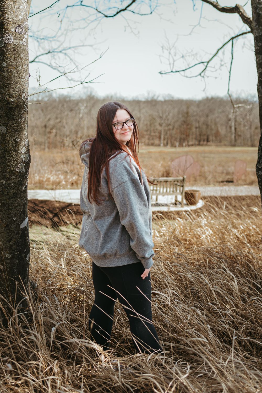 Portrait session in tall grass field with rustic barn and trees in background.