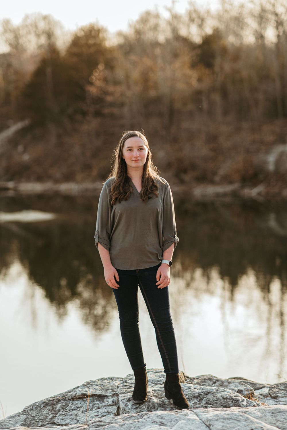 A woman stands on a rocky outcrop overlooking a serene lake at sunset.
