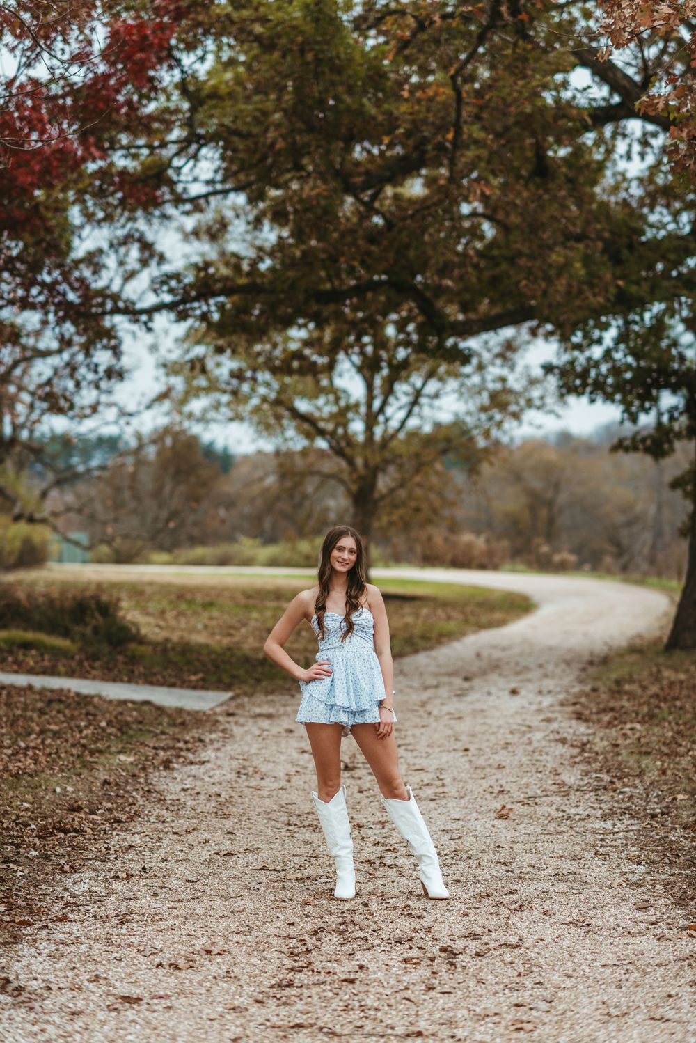 A portrait of someone in a light blue dress and white boots on a winding autumn path.