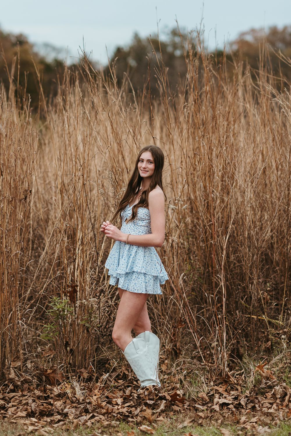 A fall photoshoot in tall grass featuring someone in a blue dress and white boots.