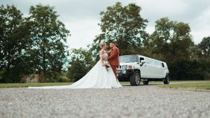 Bride and groom sharing a romantic kiss beside a white Hummer limousine on their wedding day.